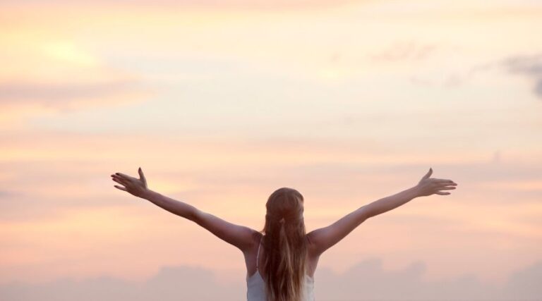 Femme qui lève les bras au ciel, heureuse de son assurance vie participative